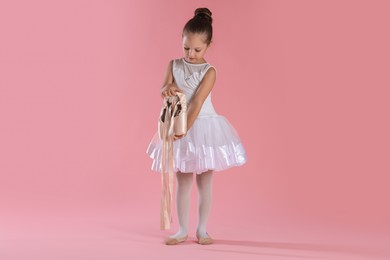 Photo of Little ballerina with pointe shoes on pink background