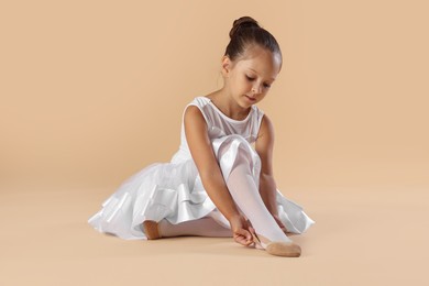 Photo of Little ballerina putting on pointe shoes against beige background