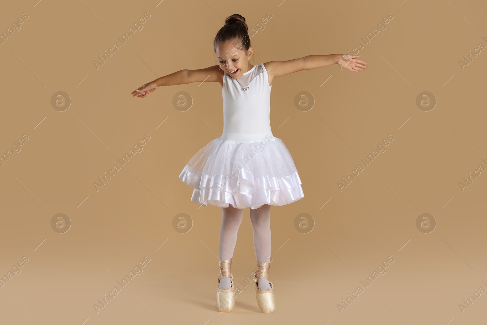 Photo of Little ballerina practicing dance moves on beige background