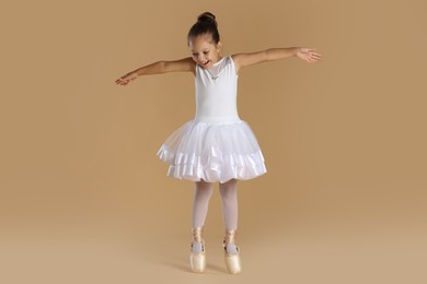 Little ballerina practicing dance moves on beige background