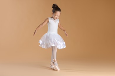 Photo of Little ballerina practicing dance moves on beige background