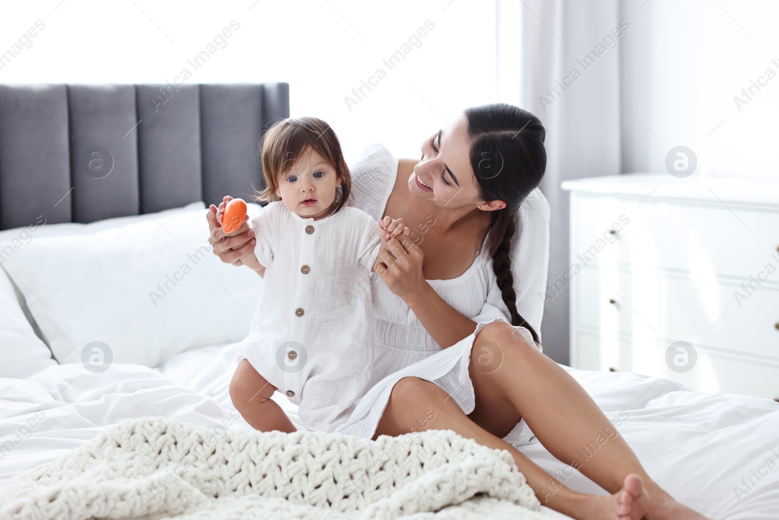 Photo of Beautiful young mother and her cute little baby with toy on bed at home