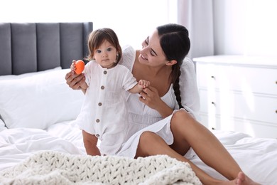 Photo of Beautiful young mother and her cute little baby with toy on bed at home