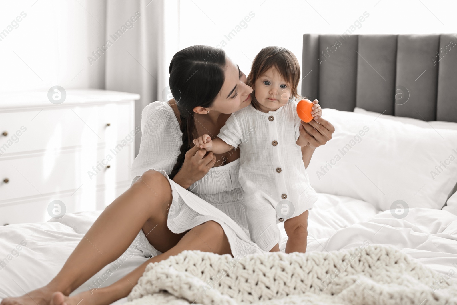 Photo of Beautiful young mother and her cute little baby with toy on bed at home