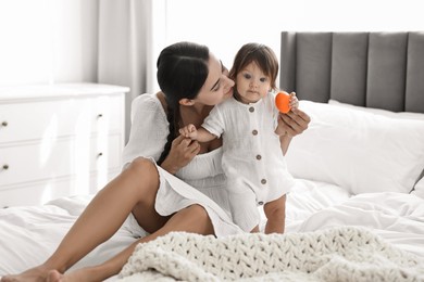 Beautiful young mother and her cute little baby with toy on bed at home