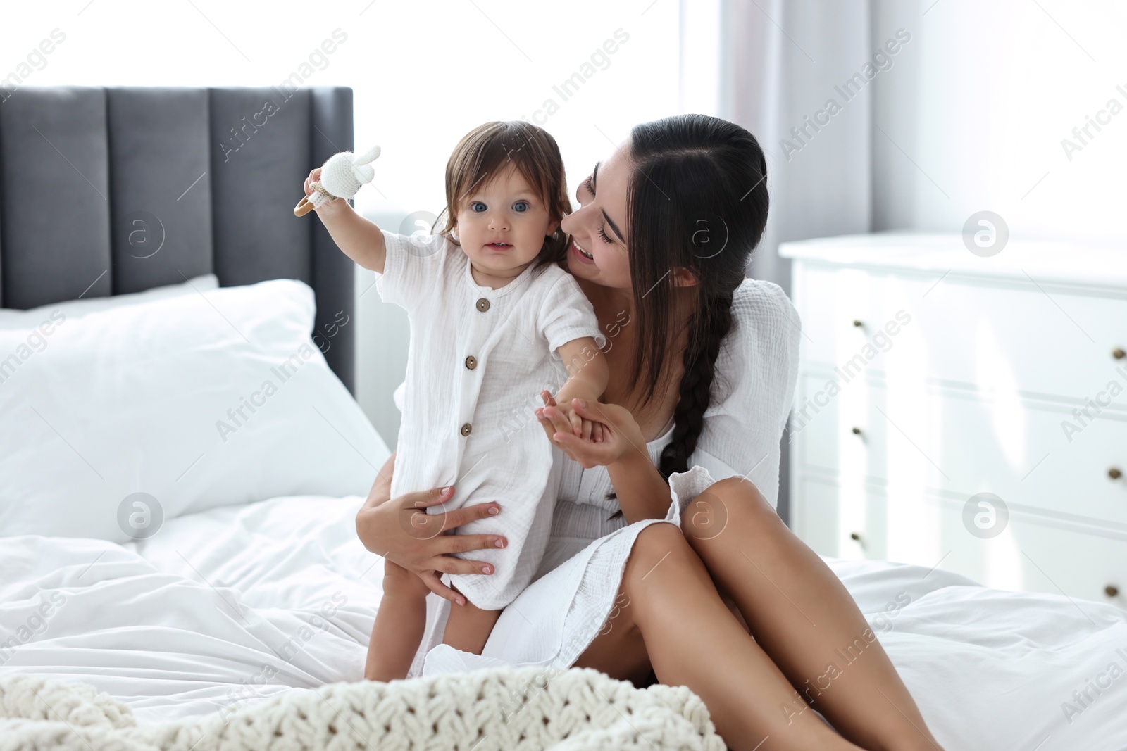 Photo of Beautiful young mother and her cute little baby with rattle on bed at home