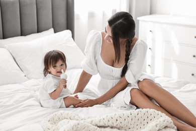 Beautiful young mother and her cute little baby with rattle on bed at home