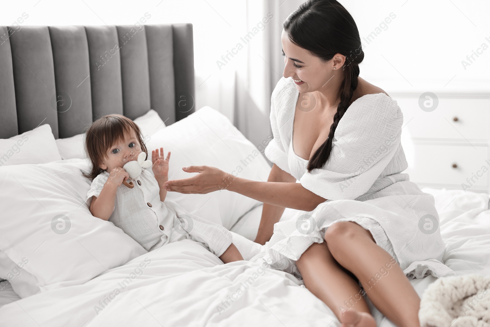 Photo of Beautiful young mother and her cute little baby with rattle on bed at home