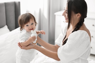 Photo of Beautiful young mother and her cute little baby with rattle on bed at home