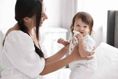 Photo of Beautiful young mother and her cute little baby with rattle on bed at home