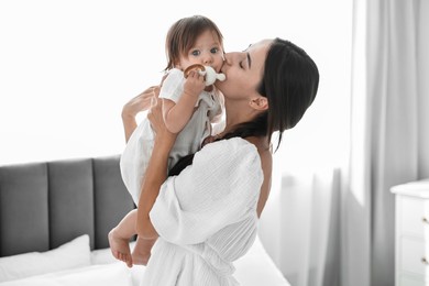 Beautiful young mother and her cute little baby with rattle in bedroom