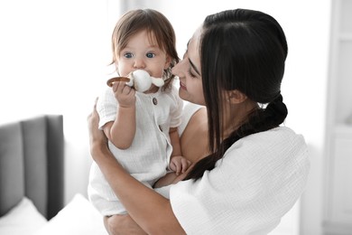 Photo of Beautiful young mother and her cute little baby with rattle indoors