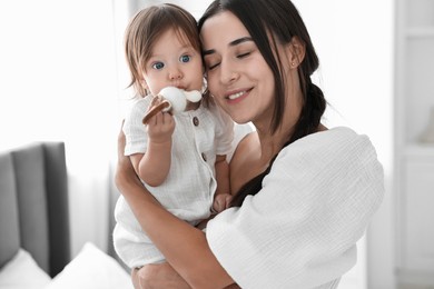 Photo of Beautiful young mother and her cute little baby with rattle indoors