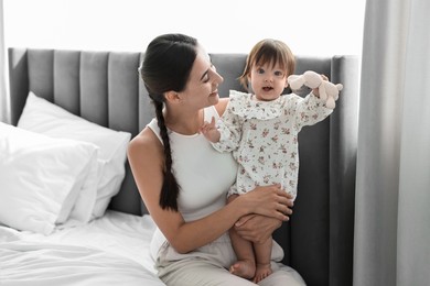 Photo of Beautiful young mother and her cute little baby with rabbit toy on bed at home