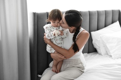 Beautiful young mother and her cute little baby with rabbit toy on bed at home