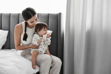 Beautiful young mother and her cute little baby with rabbit toy on bed at home, space for text