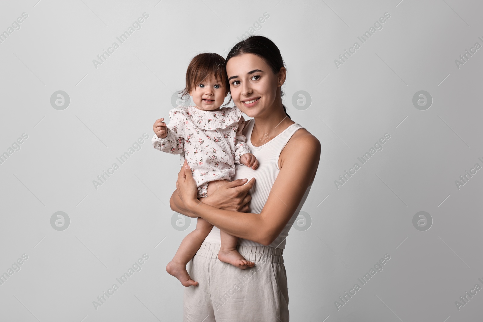 Photo of Beautiful young mother and her cute little baby on light grey background