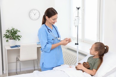 Photo of Doctor examining little girl and setting IV drip on bed at hospital