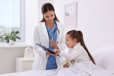 Doctor examining little girl on bed at hospital