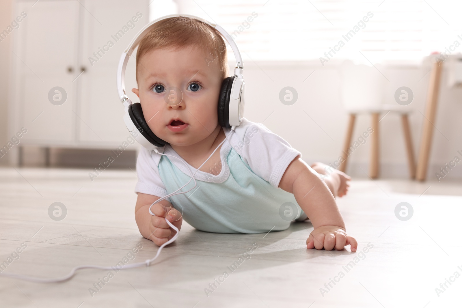 Photo of Cute little baby with headphones on floor at home