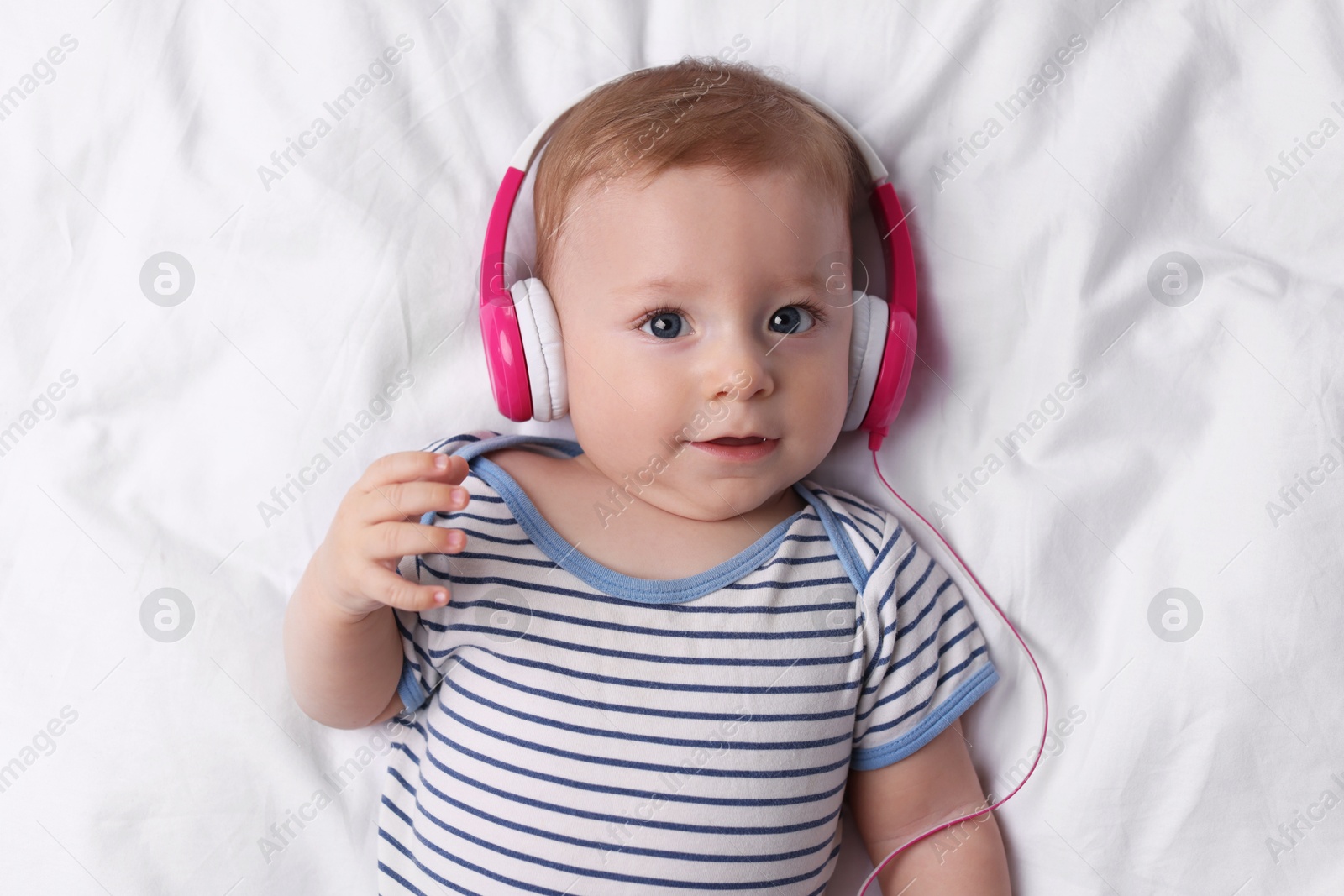 Photo of Cute little baby with headphones lying on bed, top view