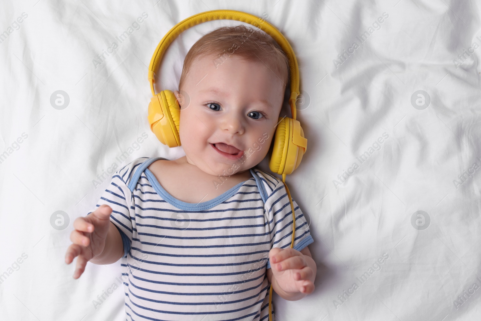 Photo of Cute little baby with headphones lying on bed, top view