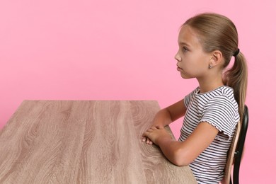 Photo of Girl with correct posture sitting at wooden desk on pink background