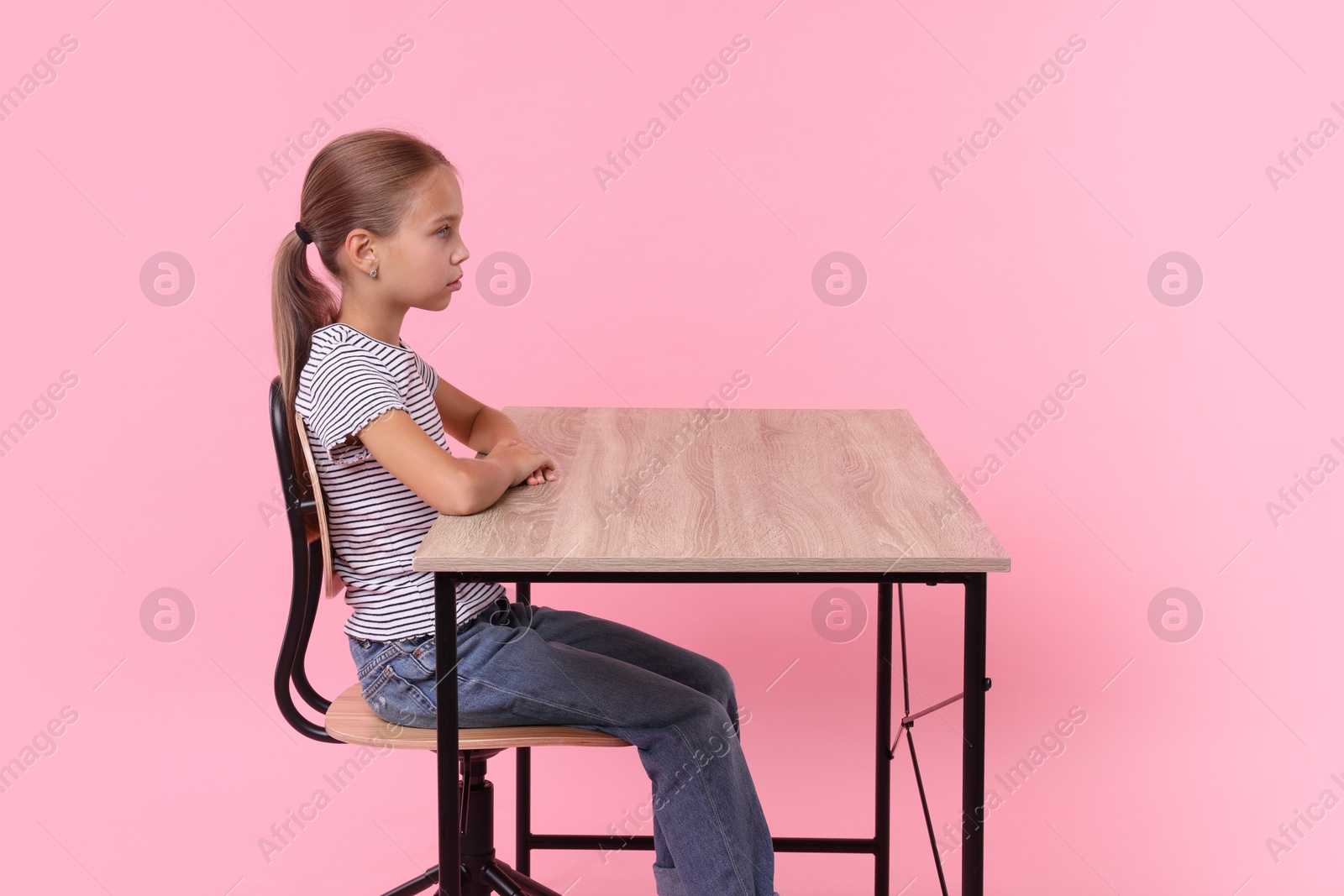 Photo of Girl with correct posture sitting at wooden desk on pink background