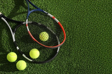 Photo of Tennis rackets and balls on green artificial grass, flat lay. Space for text