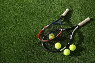 Photo of Tennis rackets and balls on green artificial grass, flat lay. Space for text