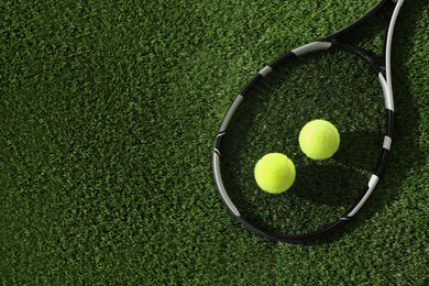 Photo of Tennis racket and balls on green artificial grass, flat lay. Space for text