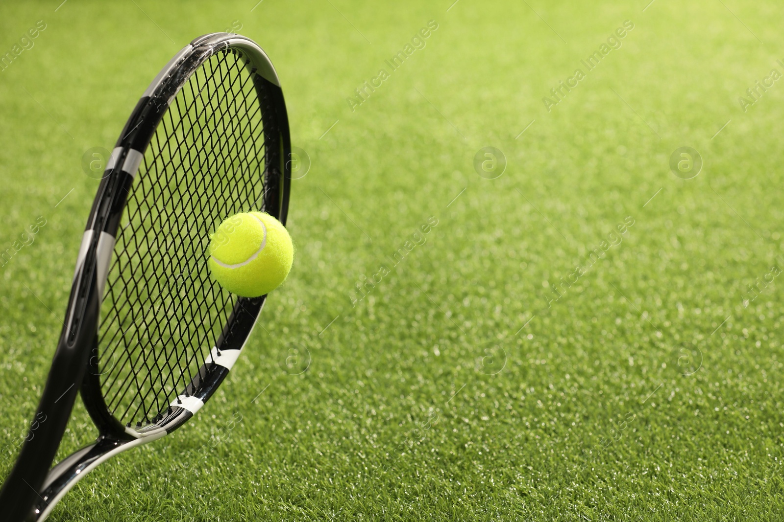 Photo of Tennis racket with ball on green artificial grass, closeup. Space for text