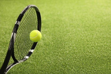 Photo of Tennis racket with ball on green artificial grass, closeup. Space for text