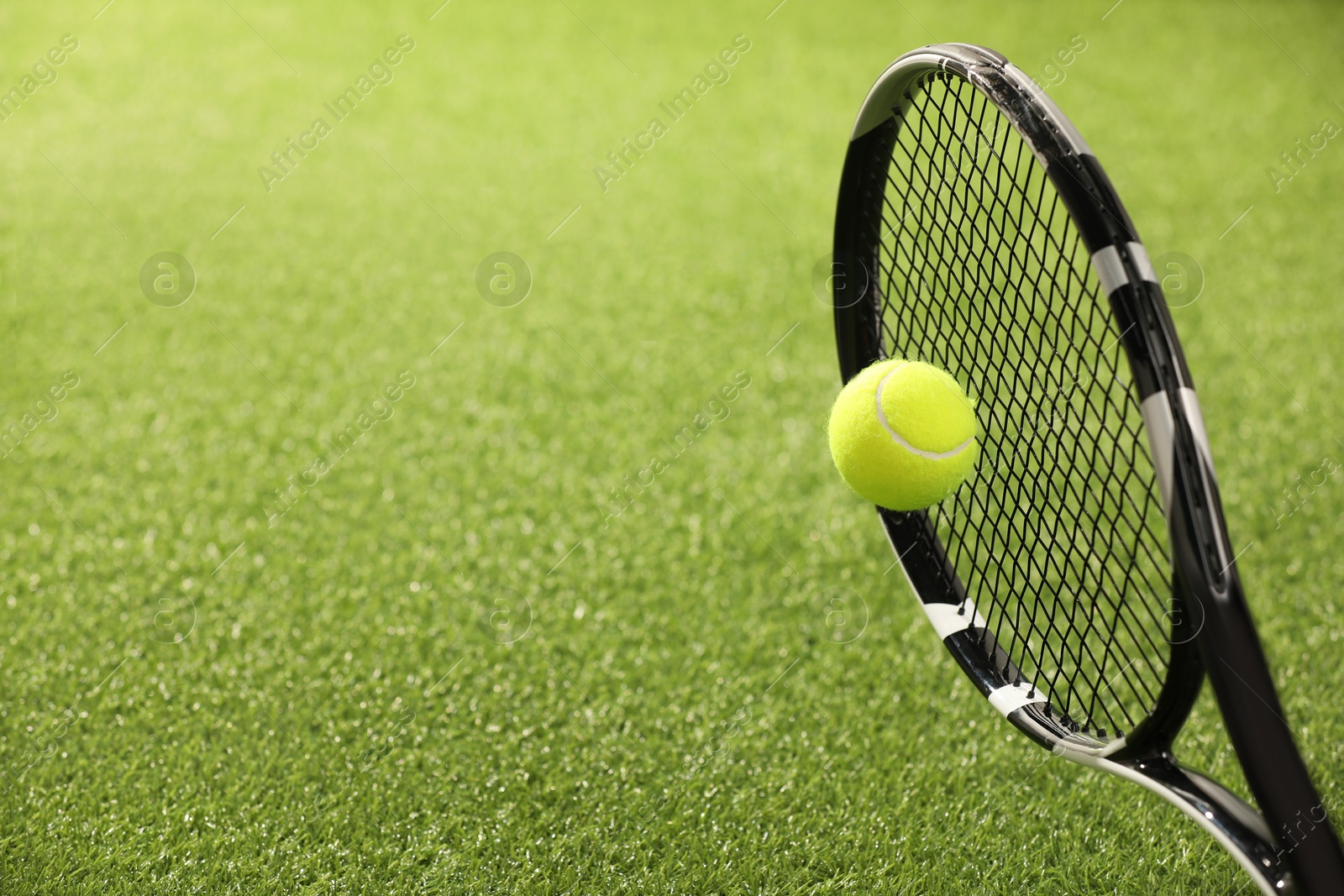 Photo of Tennis racket with ball on green artificial grass, closeup. Space for text