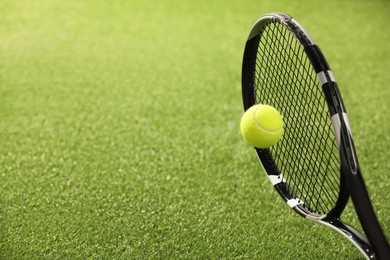 Photo of Tennis racket with ball on green artificial grass, closeup. Space for text