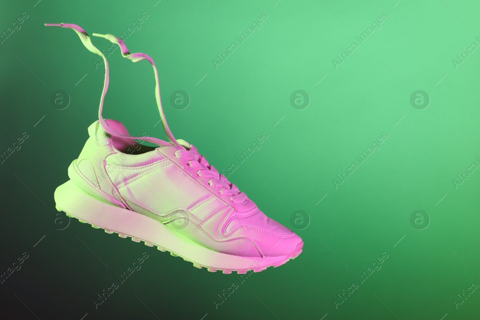 Photo of Stylish sneaker in air against green background in neon lights, space for text