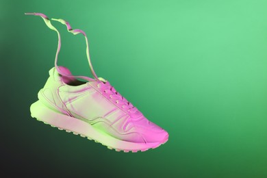 Stylish sneaker in air against green background in neon lights, space for text