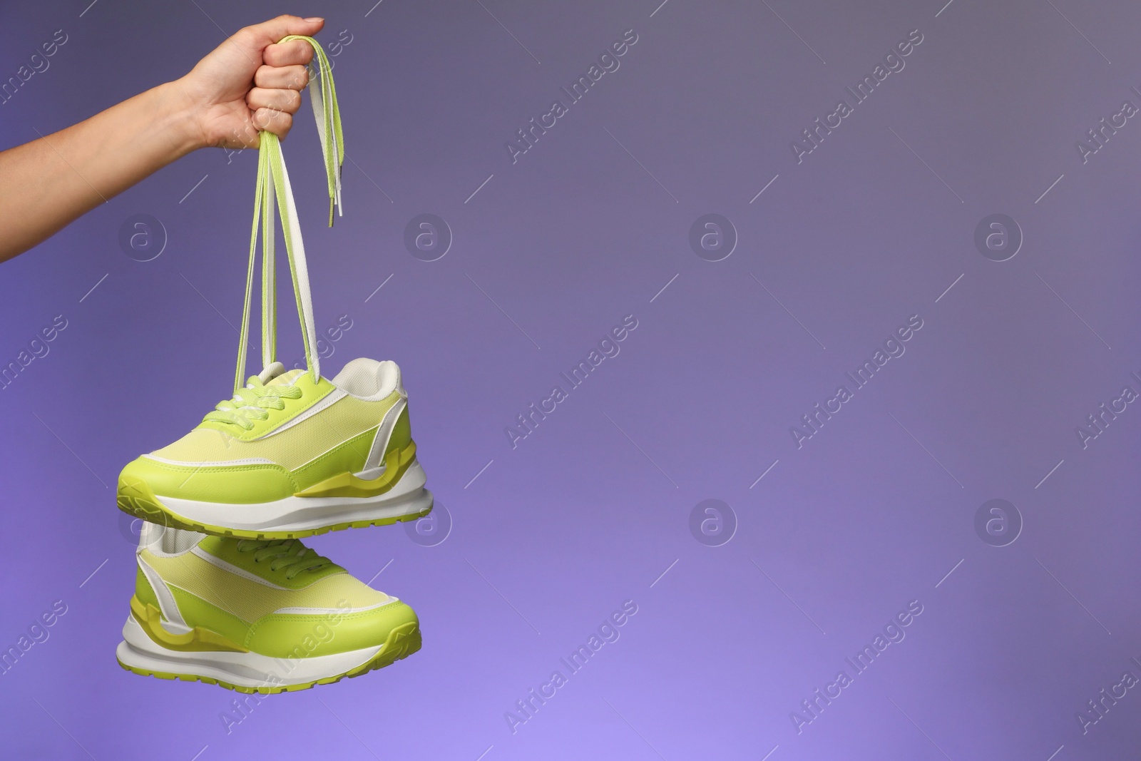 Photo of Woman holding pair of stylish sneakers against color background, closeup. Space for text