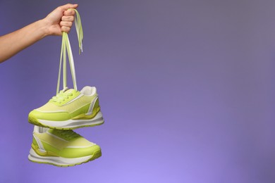 Woman holding pair of stylish sneakers against color background, closeup. Space for text