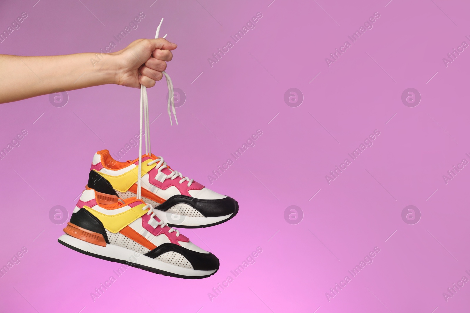 Photo of Woman holding pair of stylish sneakers against color background, closeup. Space for text