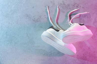 Pair of stylish sneakers against textured background in neon lights, top view. Space for text