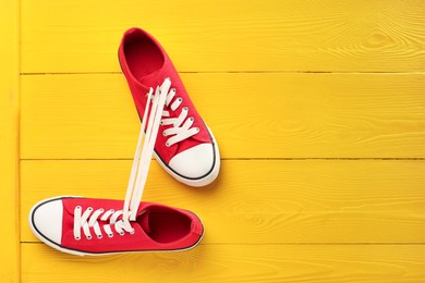 Pair of stylish sneakers on yellow wooden background, top view. Space for text