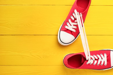 Pair of stylish sneakers on yellow wooden background, top view. Space for text