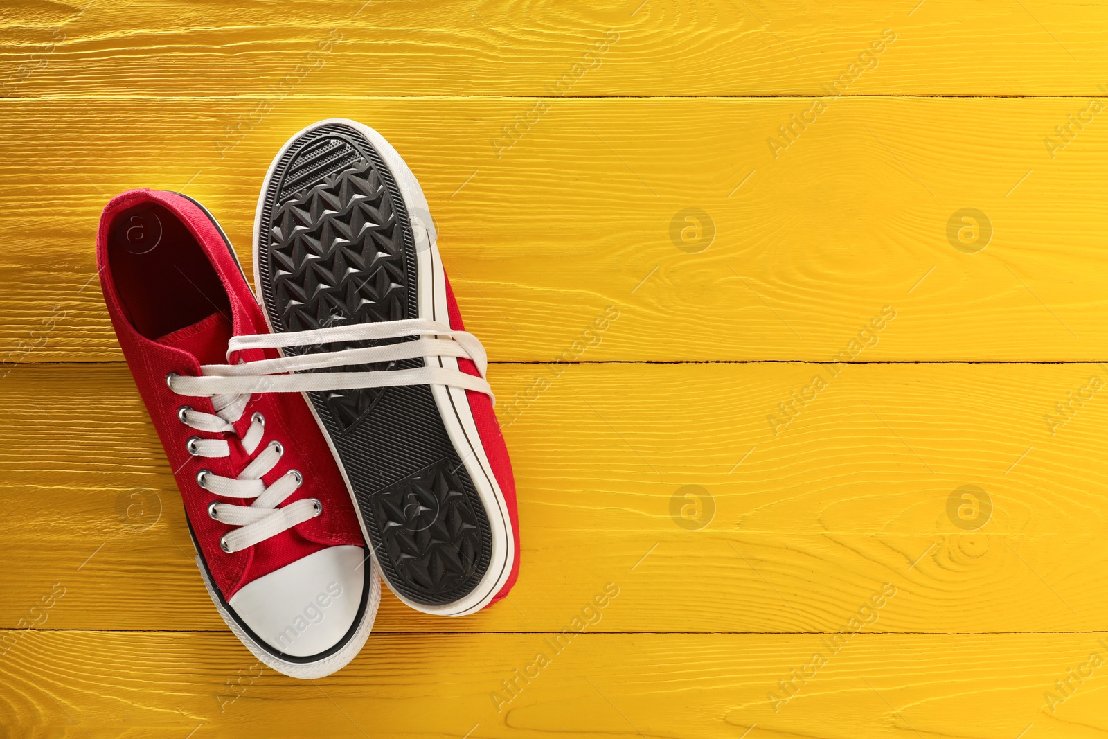 Photo of Pair of stylish sneakers on yellow wooden background, top view. Space for text