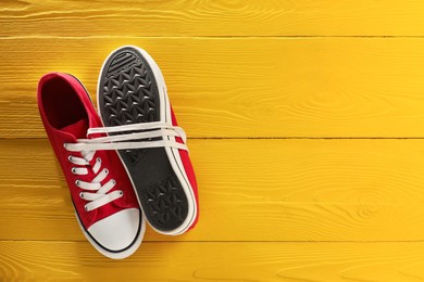 Photo of Pair of stylish sneakers on yellow wooden background, top view. Space for text