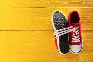 Photo of Pair of stylish sneakers on yellow wooden background, top view. Space for text