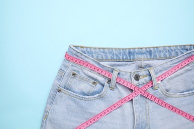 Photo of Jeans and measuring tape on light blue background, top view