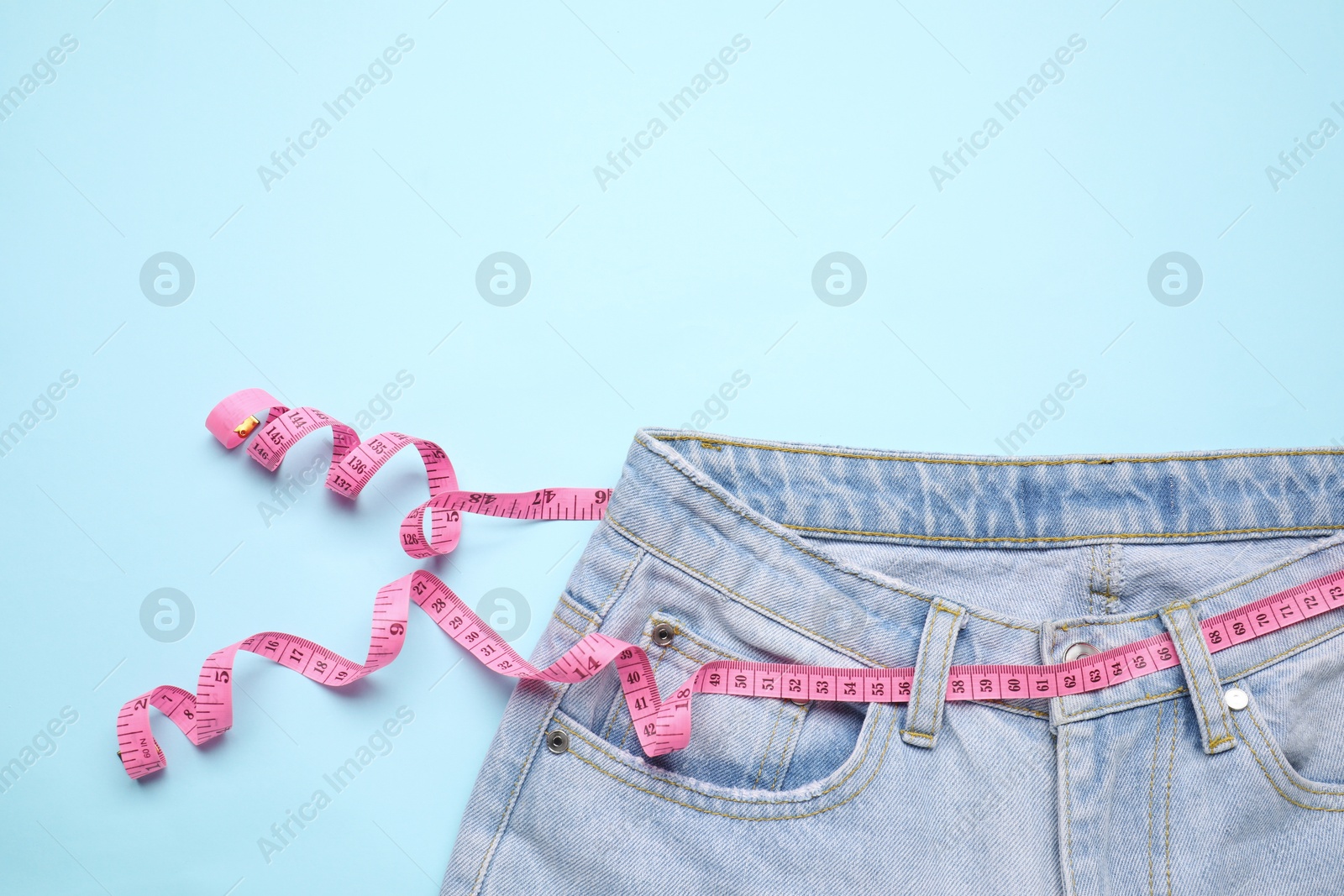 Photo of Jeans and measuring tape on light blue background, top view