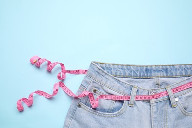 Photo of Jeans and measuring tape on light blue background, top view