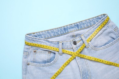 Photo of Jeans and measuring tape on light blue background, top view